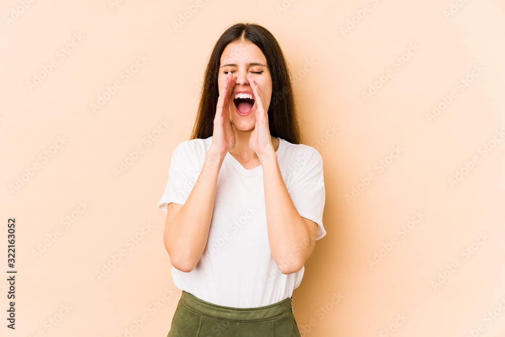 Young caucasian woman isolated on beige background shouting excited to front. Young caucasian woman isolated on beige background shouting excited to front.
