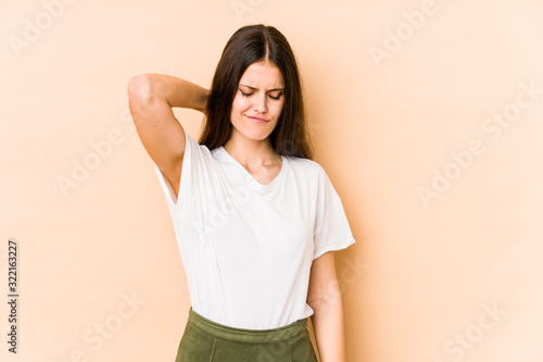 Young caucasian woman isolated on beige background suffering neck pain due to sedentary lifestyle.