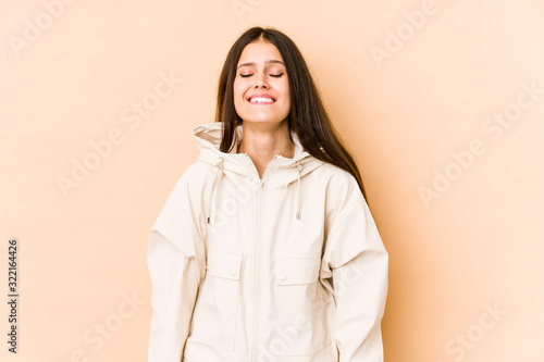 Young caucasian woman isolated on beige background laughs and closes eyes, feels relaxed and happy.