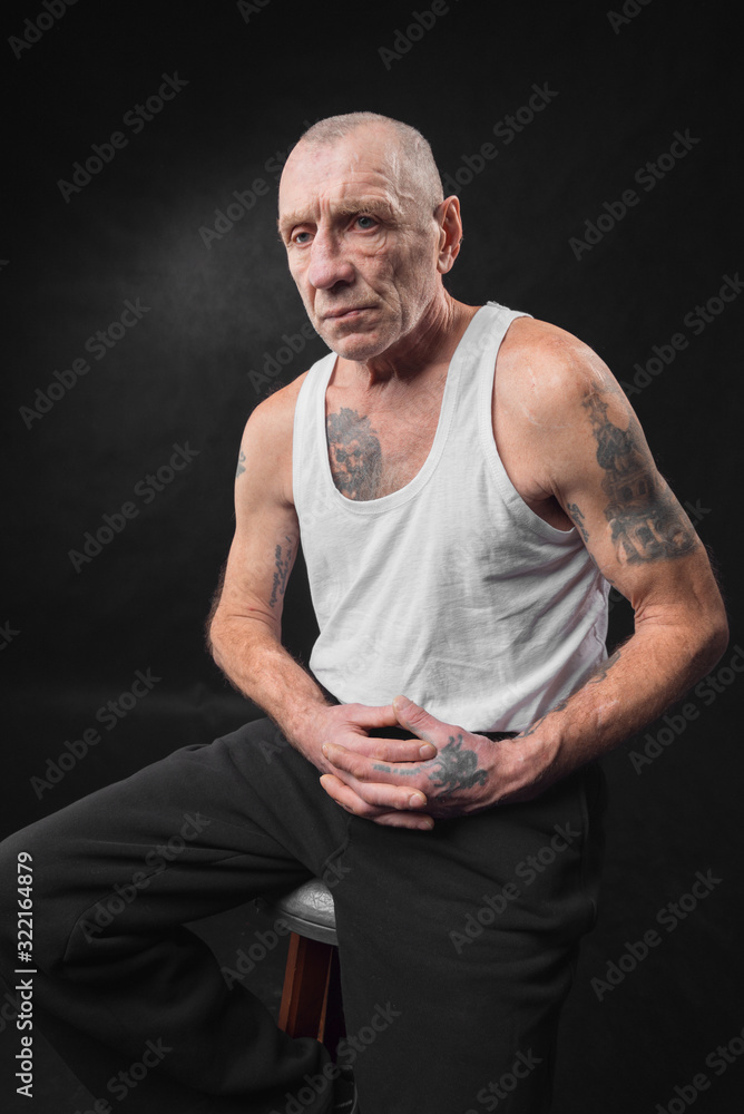Old man with tattoos is sitting on a chair. Stock Photo | Adobe Stock