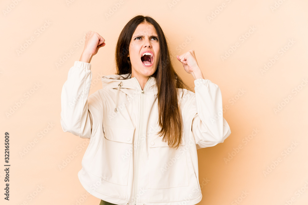 Young caucasian woman isolated on beige background raising fist after a victory, winner concept. Young caucasian woman isolated on beige background raising fist after a victory, winner concept.