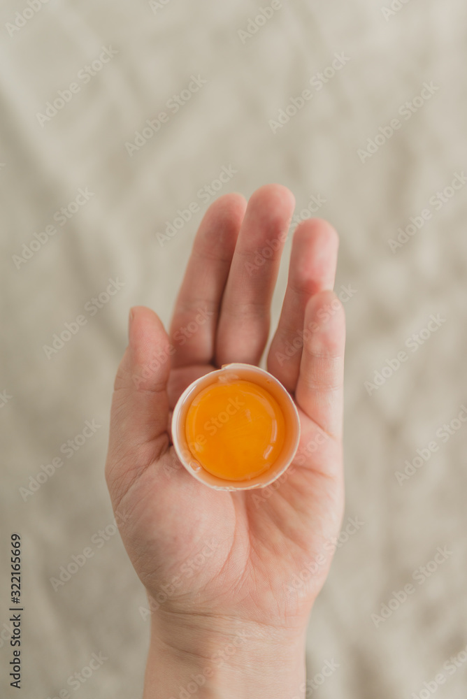 The hand of a young woman holds a broken chicken egg. Top view of an egg and yolk. Food concept. The hand of a young woman holds a broken chicken egg. Top view of an egg and yolk. Food concept.