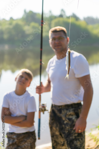 Such a small fish. Father and son stretching a fishing rod with fish on the hook while little boy looking sad.