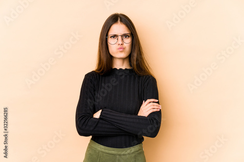 Young caucasian woman isolated on beige background blows cheeks, has tired expression. Facial expression concept. © Asier
