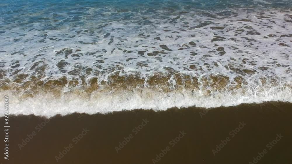 Aerial view of a small wave rolling over a sandy beach. Aerial view of a small wave rolling over a sandy beach.