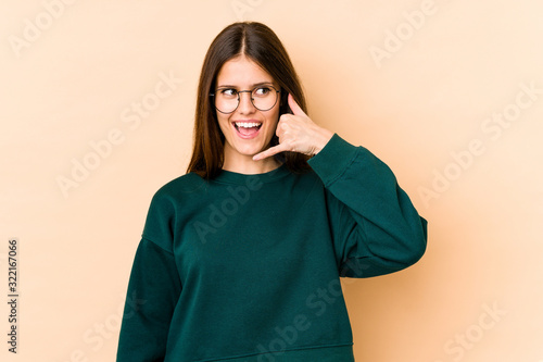 Young caucasian woman isolated on beige background showing a mobile phone call gesture with fingers. © Asier