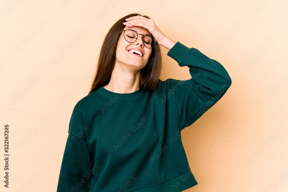 Young caucasian woman isolated on beige background laughs joyfully keeping hands on head. Happiness concept. Young caucasian woman isolated on beige background laughs joyfully keeping hands on head. Happiness concept.