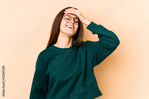 Young caucasian woman isolated on beige background laughs joyfully keeping hands on head. Happiness concept. © Asier