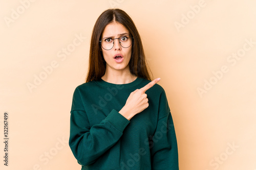 Young caucasian woman isolated on beige background pointing to the side © Asier