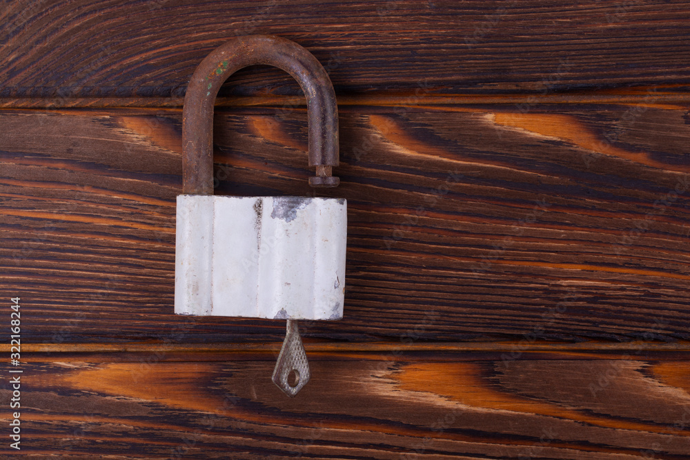 Fototapeta premium Old rusty lock with a key on a wooden board. Free space for an inscription.