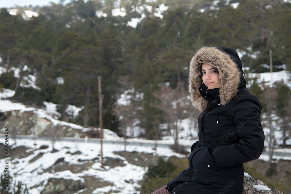 Portrait of a young happy and beautiful teenage girl dressed in winter clothing at a snowy mountain