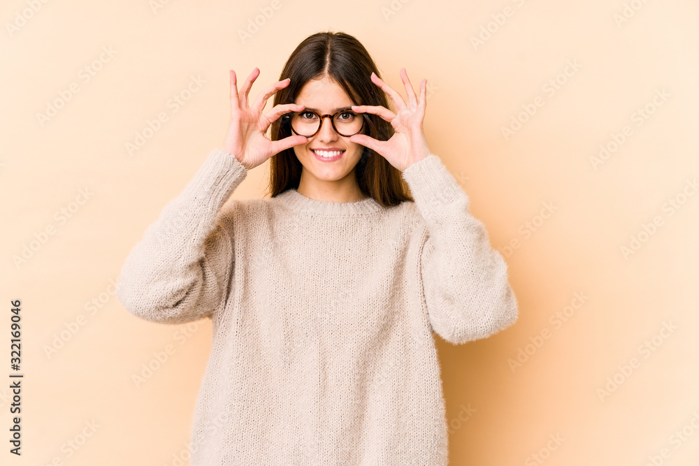 Young caucasian woman isolated on beige background showing okay sign over eyes Young caucasian woman isolated on beige background showing okay sign over eyes
