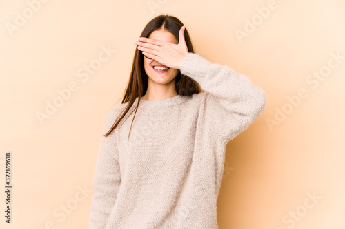 Young caucasian woman isolated on beige background covers eyes with hands, smiles broadly waiting for a surprise.