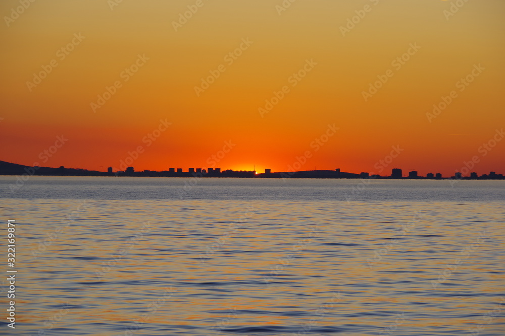 Naklejka premium A romantic sunset against the background of the orange sky and fantastic glimpses of the reflecting sun in the bluish-gray water. An evening that is impossible to forget.