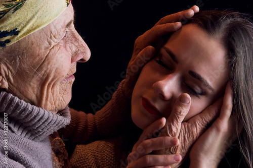 Young granddaughter in the arms of her grandmother. Old grandmother hugs a young girl close-up. Grandmother's wrinkled hands on the girl's cheeks.