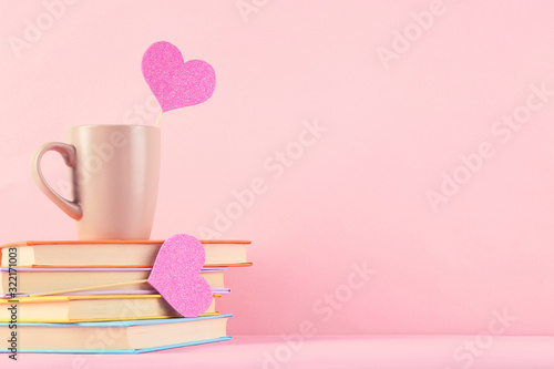 Paper hearts with cup and stack of books on pink background