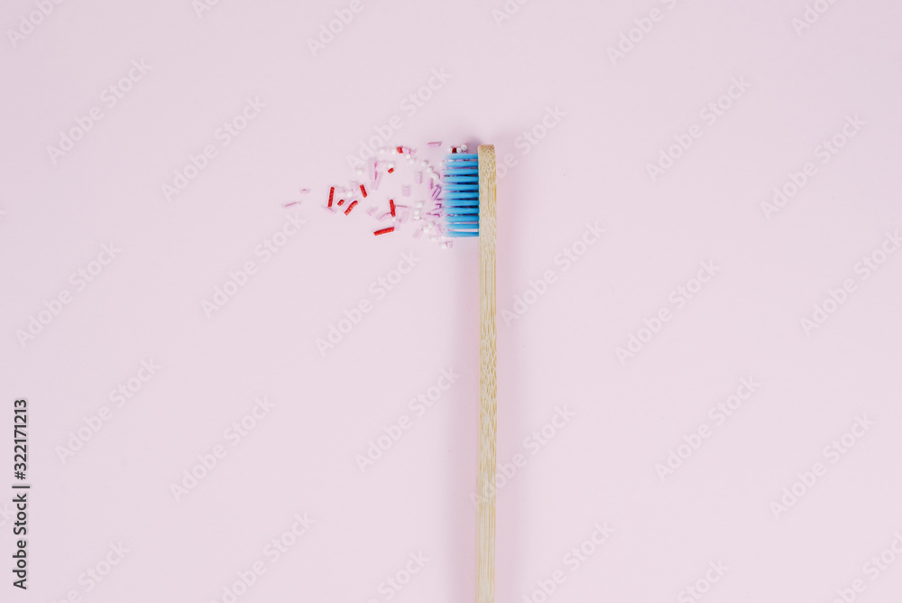Bamboo wooden toothbrush with blue bristles next to sugar sprinkles on a pink background. The concept of oral care and unhealthy lifestyle. Tooth decay due to sugar Bamboo wooden toothbrush with blue bristles next to sugar sprinkles on a pink background. The concept of oral care and unhealthy lifestyle. Tooth decay due to sugar