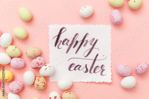Inscription HAPPY EASTER letters candy chocolate eggs and jellybean sweets isolated on trendy pastel pink background. Simple minimalism flat lay top view copy space © Юлия Завалишина