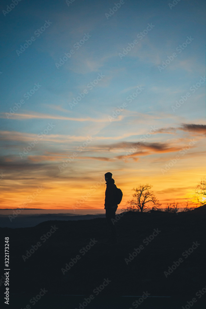 Vertical image of traveler man enjoying epic sunset in mountains, silhouette of young man trekking during beautiful suset in mountains, harmony with nature