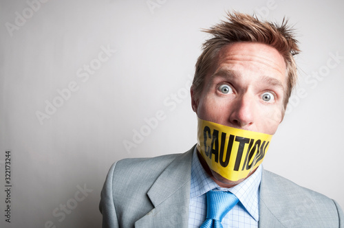 Shocked businessman gagged with yellow caution tape