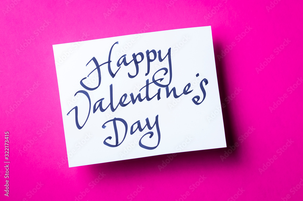 Handwritten Happy Valentine's Day message in simple calligraphic script on white card sitting on bright pink background Handwritten Happy Valentine's Day message in simple calligraphic script on white card sitting on bright pink background