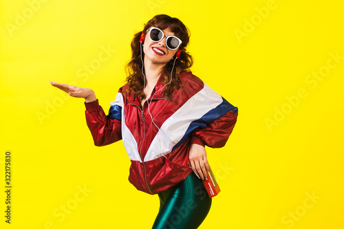 Cheerful gorgeous girl in clothes in the style of the 90s, with a vintage cassette player and headphones, in the studio on a white background. Music, emotions, fashion