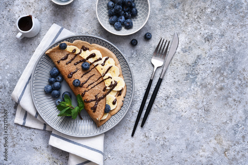 Crepe with banana, chocolate sauce and blueberries for breakfast on a stone background. photo