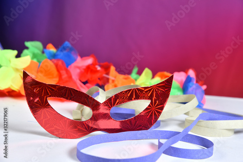 red carnival costume mask in colorful confetti and streamers on pink background with space for text