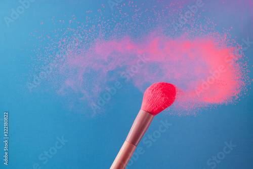 close-up photo of two professional make-up brushes with pink powder in motion on blue background