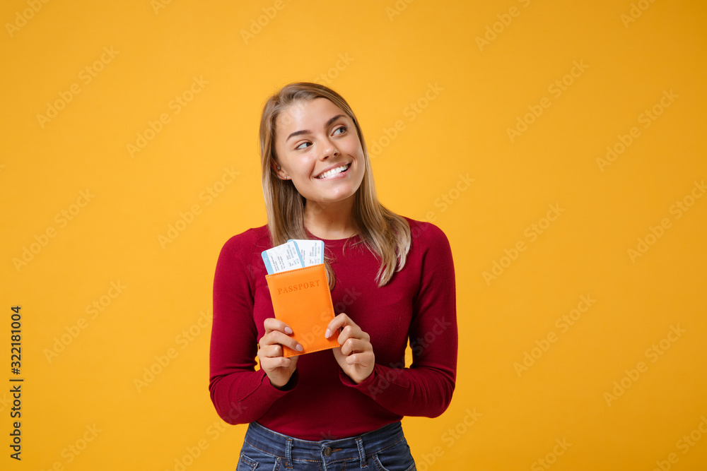 Smiling pensive young blonde woman girl in casual clothes posing isolated on yellow orange background in studio. People lifestyle concept. Mock up copy space. Hold passport tickets, looking aside up. Smiling pensive young blonde woman girl in casual clothes posing isolated on yellow orange background in studio. People lifestyle concept. Mock up copy space. Hold passport tickets, looking aside up.