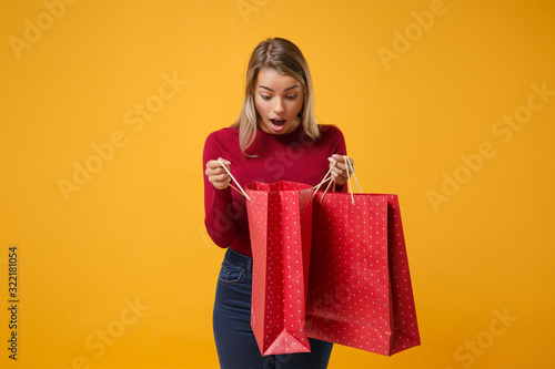 Shocked young blonde woman girl in casual clothes posing isolated on yellow orange background in studio. People lifestyle concept. Mock up copy space. Hold package bag with purchases after shopping.