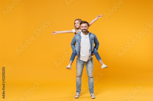 Funny bearded man with child baby girl. Father little kid daughter isolated on yellow background. Love family parenthood childhood concept. Giving piggyback ride to joyful sit on back spreading hands.