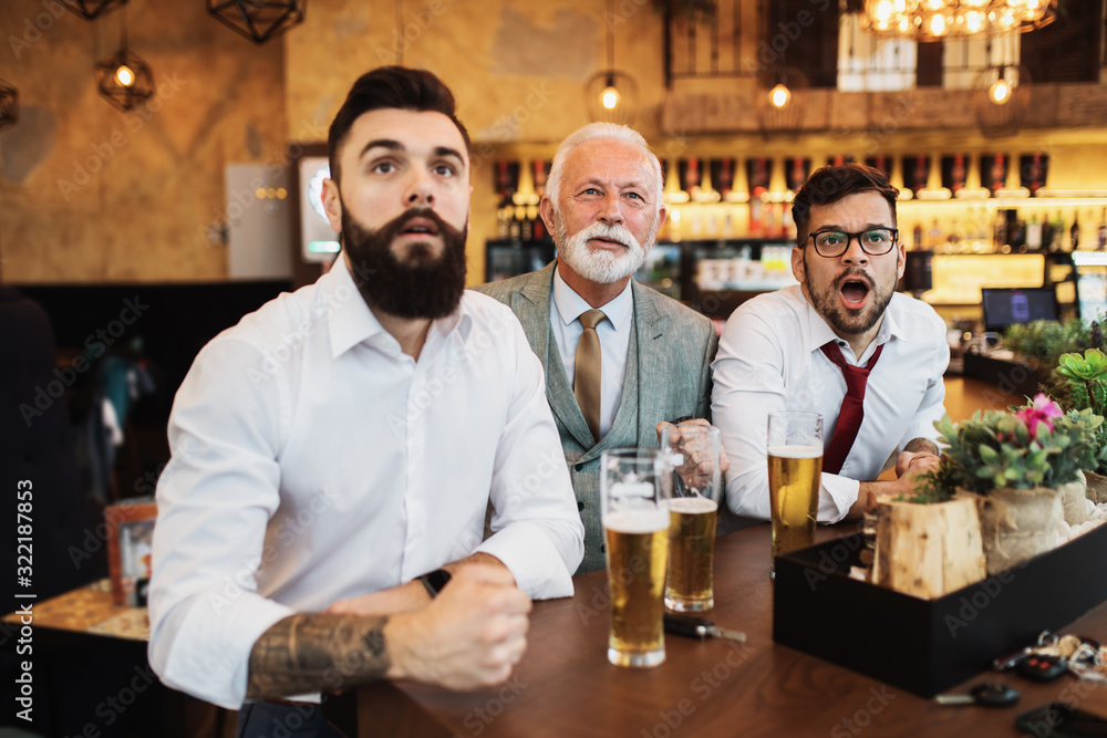  Three businessmen cheering while watching football match in a cafe bar.