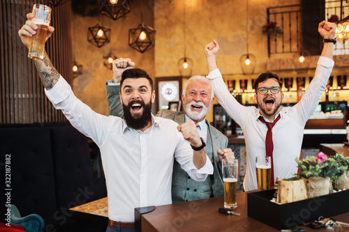  Three businessmen cheering while watching football match in a cafe bar.