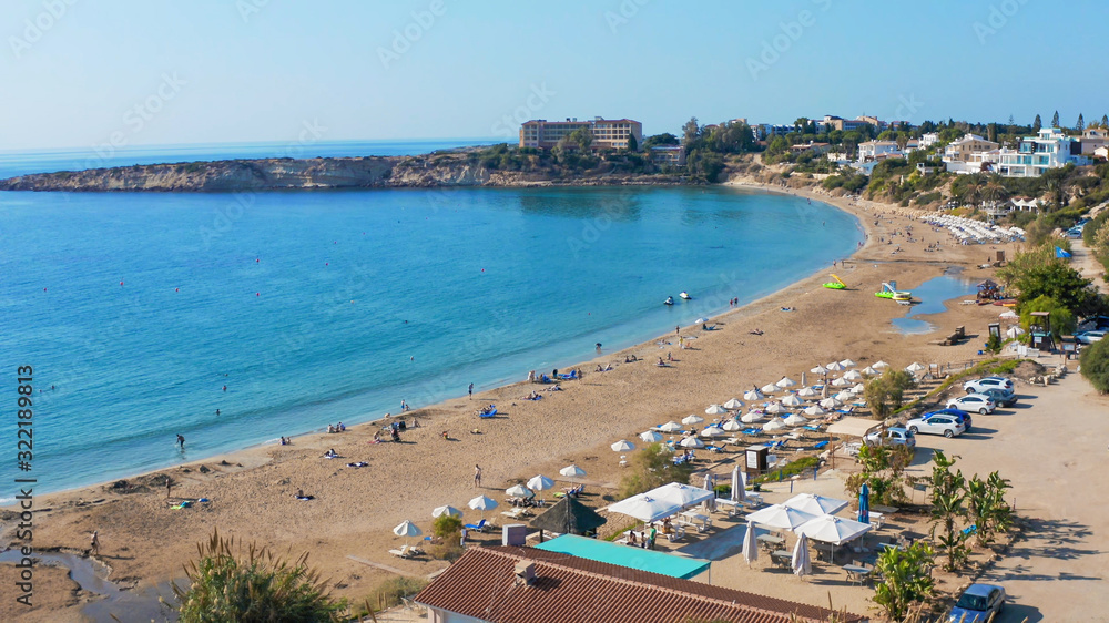 Coral Bay beach - popular beach with clear sea water and comfortable sandy beach, many tourists, sunbeds with umbrellas in Peyia village, Cyprus, aerial view.