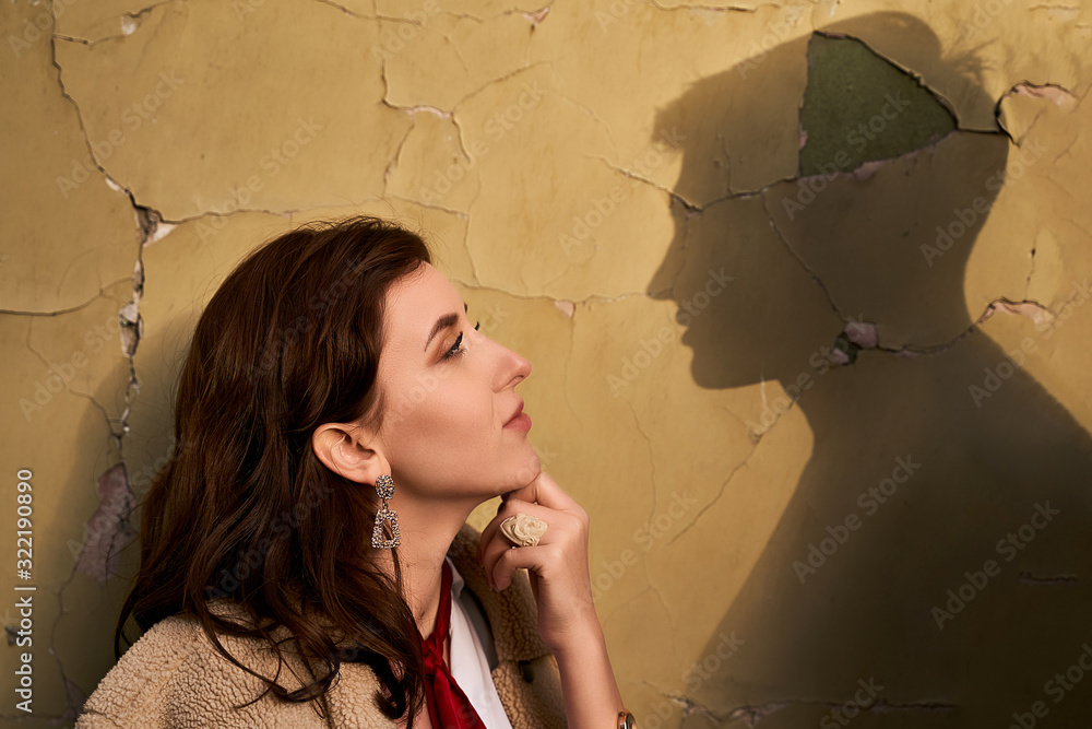 Beautiful young redhead woman wearing teddy jacket and white shirt and red neckpiece is thinking of her ideal boyfriend man or lover represented by a shadow on the wall