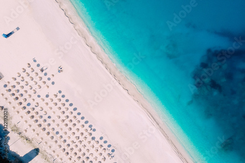 Top-down aerial view of a clean beach equipped with umbrellas and sunbeds on the turquoise sea. Greece.