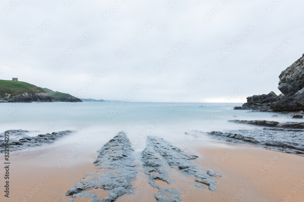 A long exposure photo of a beach with a rocks in the foreground