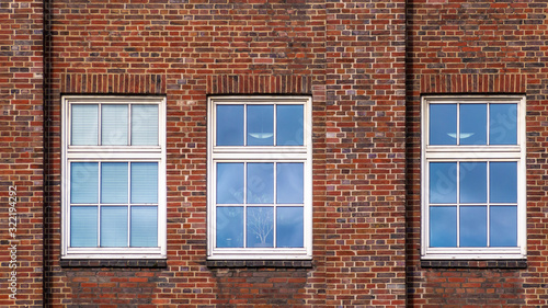 One in three is different: Brick wall with three windows reflecting the sky.
