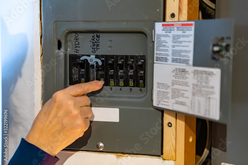 Canadian house distribution board, circuit breaker panel with interchangeable circuit breakers. woman's hand pointing and clicking on a breaker. photo