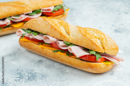 Two Long baguette Sandwiches with arugula, slices of fresh tomatoes, ham and cheese