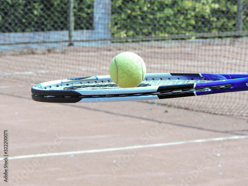 Pelota de tenis en movimiento con fondo natural acompañado con una raqueta en cancha de tenis