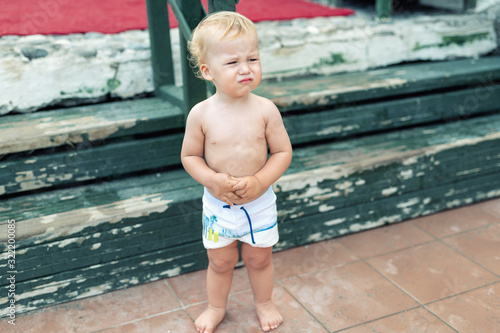 Fotografi Cute funny upset caucasian 2 year old toddler boy standing abandoned alone at beach summer day
