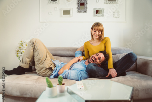 Happy couple laughing having fun at home watching television on the sofa.