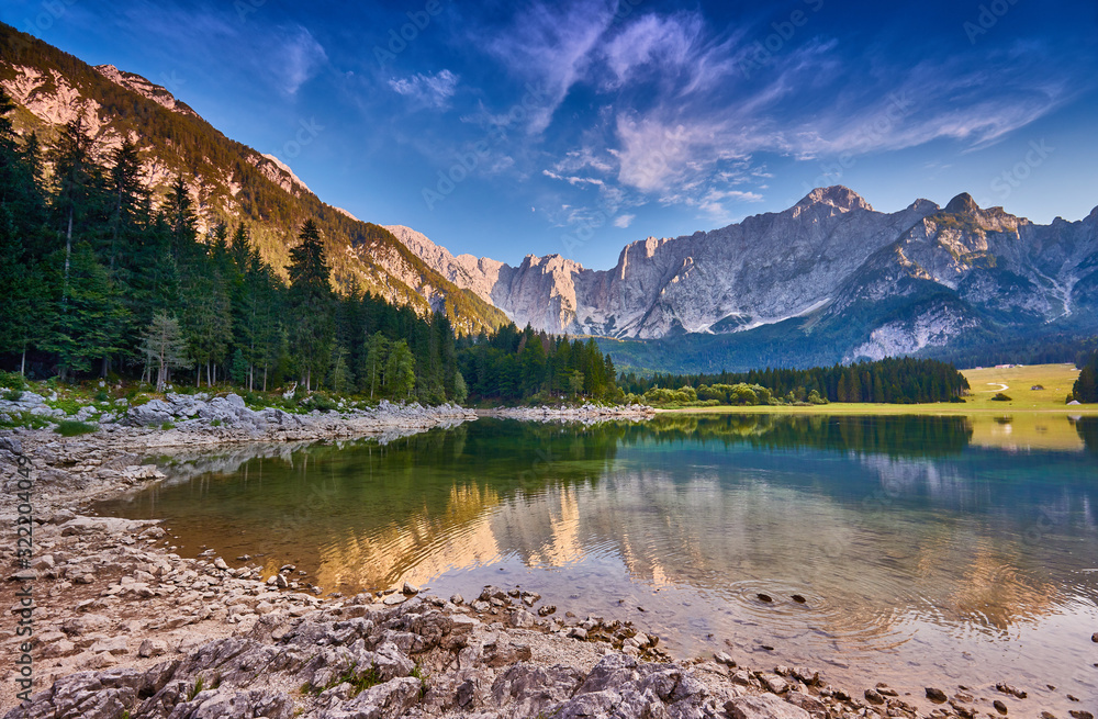 Amazing view on Lago di Fusine Inferiore at sunrise. Splendid morning scene of Julian Alps, Province of Udine, Italy, Europe. Beautiful forests are reflected in the quiet lake. Dolomites mountains.