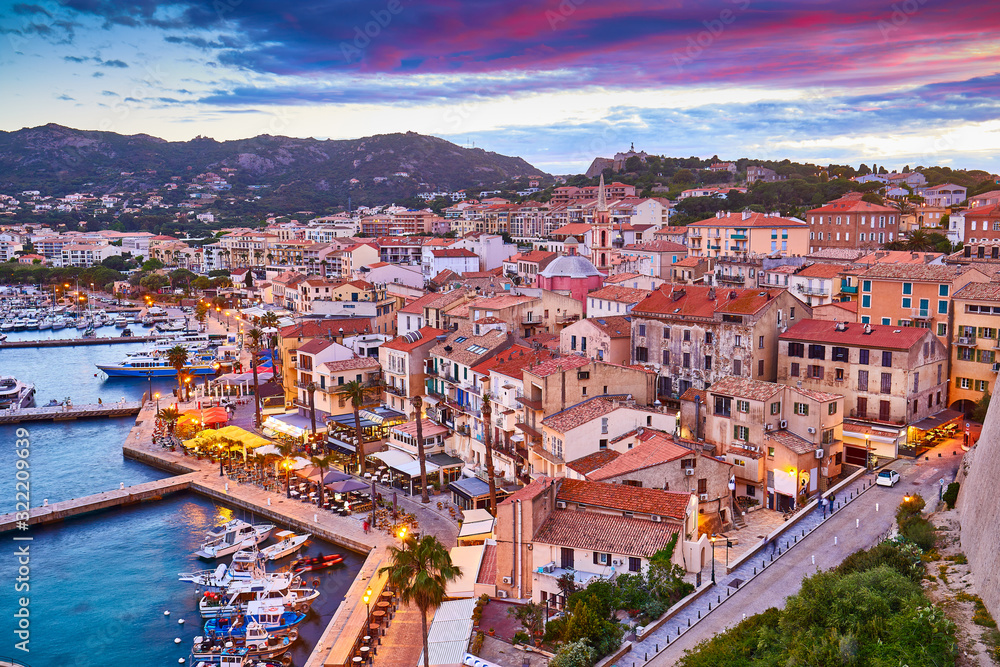 View from the walls of the citadel of Calvi on the old town with historic buildings at evening sunset. Bay with yachts and boats. Luxurious marina and popular tourist destination. Corsica, France