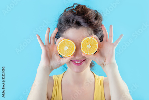 Beautiful brunette in yellow top holds orange like eyes over blue background, beauty concept photo