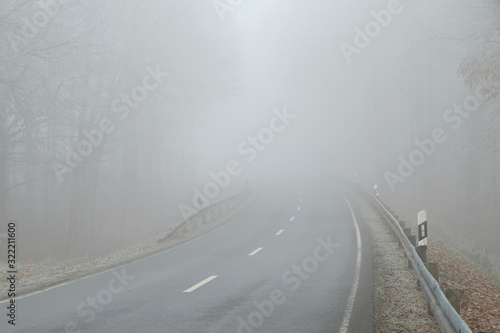 Driving on a gray and heavy foggy day on country road. Poor visibility condition. Difficult and dangerous hazard for drivers. Drive safely in autumn  and in winter.