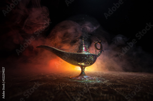 Lamp of wishes concept. Antique Aladdin arabian nights genie style oil lamp with soft light white smoke, Dark background.