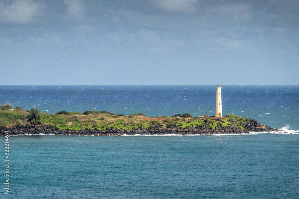 Nawiliwili, Kauai, Hawaii, USA. - January 17, 2020: Yellow Ninini lighthouse on black ocean-shore rocks of its green lands end. Blue ocean and sky..